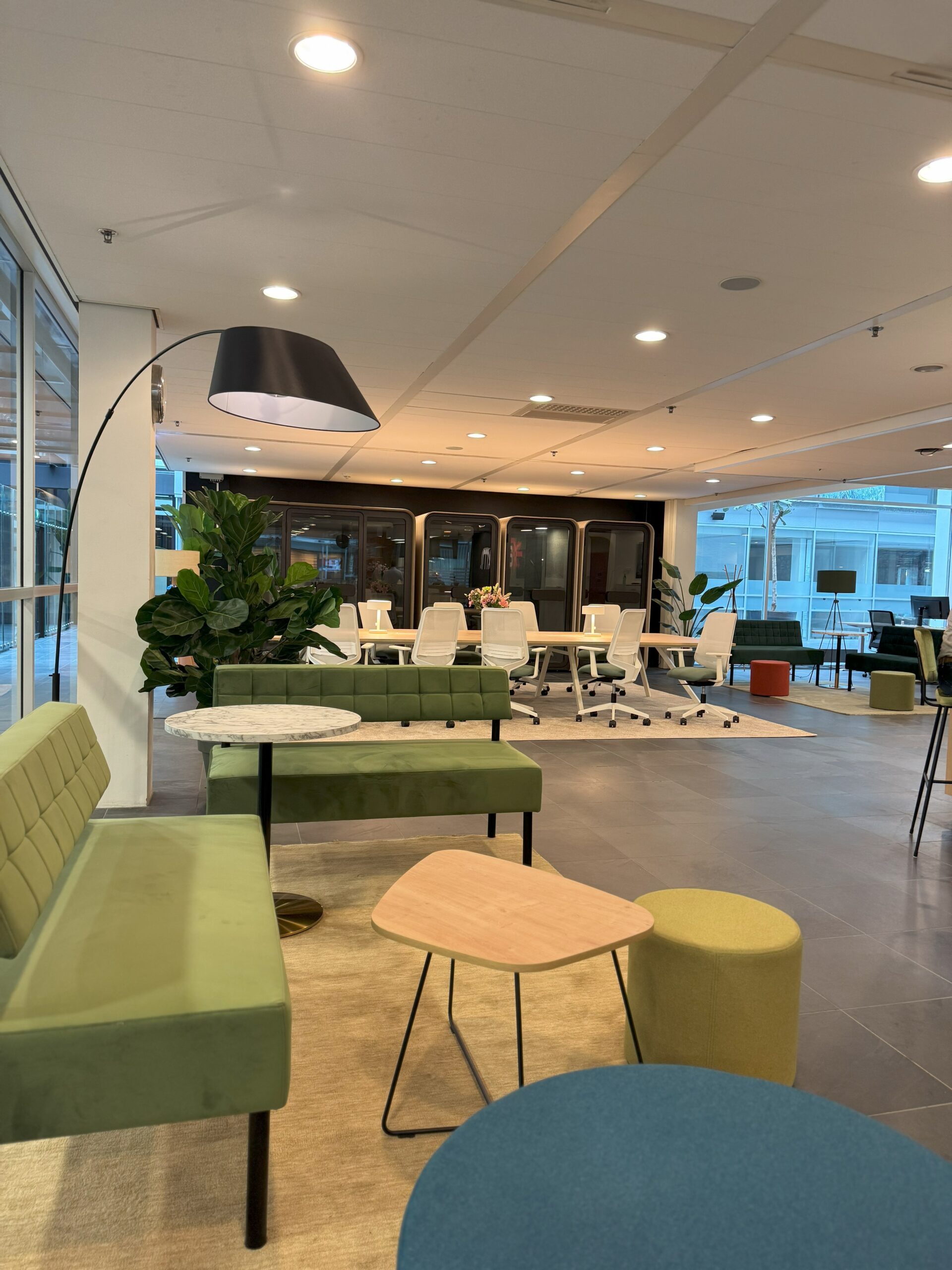 Moderne kantoorruimte met groene banken, stilte cabines en samenwerktafel en stoelen.